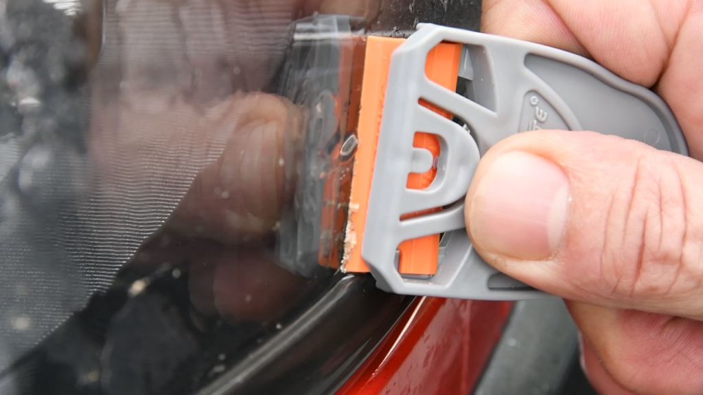 Close-up of a plastic razor blade cleaning a vehicle headlight surface